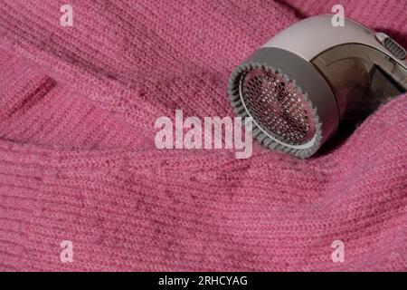 Anti-Pilling-Rasierer. Gerät zum Rasieren von Kleidung. Anti-Plush-Rasierer. Elektrischer tragbarer Pullover, Pille, Entfärbung, Fusselentferner aus pinkfarbenem Acryl- oder Wollpullover. Elektrorasierer nach der Reinigung und aufgefangenen Fusseln. Ein Pullover aus der Nahaufnahme. Alte gebrauchte Kleidung mit Pillen. Stockfoto