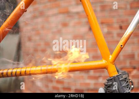 Manuelle Fahrradrenovierungsarbeiten, Lackentfernung durch Brennerfeuer, um die Farbe eines Fahrradrahmens zu ändern. Nahaufnahme. Stockfoto