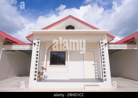 Kleines Haus, rote Dachziegel, blauer Wolkenhintergrund, ein kleines Haus. Stockfoto