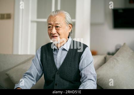 Ein trauriger älterer asiatischer Mann, der zu Hause auf der Couch saß und weinte Stockfoto