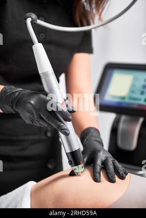 Nahaufnahme der Hände des Kosmetikers mit einem Radiofrequenz-Mikroneedling beim Entfernen von Dehnungsstreifen am weiblichen Gesäß. Frau mit Hautstraffung in der Schönheitsklinik. Stockfoto