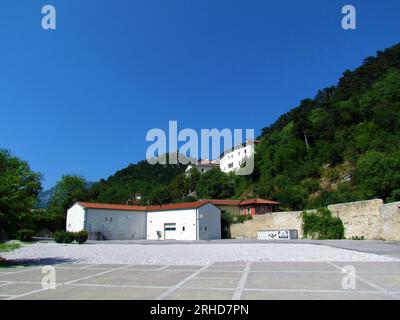 Breiter offener Platz in der Stadt Vipava mit einem weißen Fassadengebäude und einer alten Steinmauer und waldbedeckten Hängen über dem Platz in Littoral regio Stockfoto