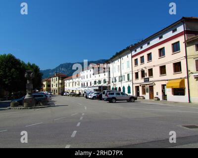 Platz im Stadtzentrum von Vipava in der slowenischen Littoral-Region mit Autos, die auf der Straße geparkt sind und die von Sonnenlicht beleuchtet werden Stockfoto