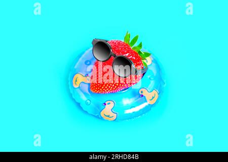 Saftige Erdbeere, verziert mit stilvoller schwarzer Sonnenbrille, schwimmt anmutig in einem Poolring. Hot Summer Escape-Konzept. Stockfoto