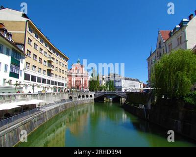 Der Fluss Ljubljanica fließt durch die slowenische Stadt Ljubljana und die Franziskanerkirche der Verkündigung und spiegelt die Gebäude im ri wider Stockfoto