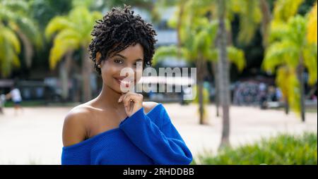 Hübsche afroamerikanische junge Erwachsene Frau mit lockigem Haar im Freien mit Palmen Stockfoto