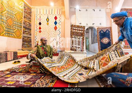 Berbermänner zeigen handgefertigte Teppiche zum Verkauf auf einem Markt, Atlasgebirge, Provinz Ouarzazate, Marokko Stockfoto