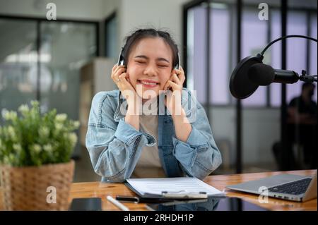 Eine hübsche und fröhliche asiatische Radiomoderatorin oder DJ mit Kopfhörern hört während ihrer Live-Radiosendung im Studio Musik. Stockfoto