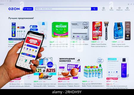 Adygea, Russland - 9. August 2023: Handwerker mit Smartphone, der Einkäufe im Ozon Online-Shop über eine mobile Anwendung vor dem Hintergrund von tätigt Stockfoto