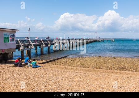 Die Leute saßen am Strand und genossen das sonnige Wetter in der Nähe der Pier in Yarmouth, Isle of Wight, England, Großbritannien Stockfoto