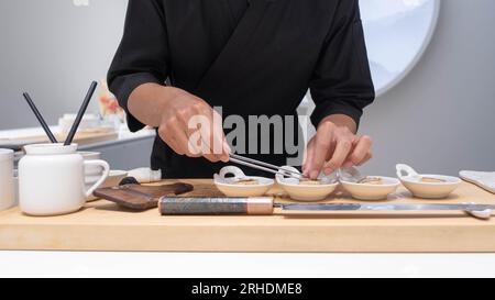 Professioneller Koch bereitet frische Fischzutat auf dem Tisch mit Messer für köstliches Sushi und Sashimi zu und bereitet sie zu, eine Person, die Luxus macht Stockfoto