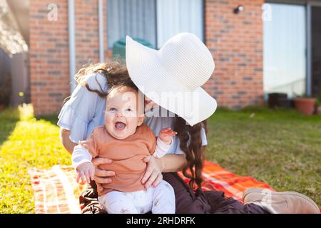 Ich war begeistert, dass das Baby draußen auf einem Picknickteppich mit Mama im Wintersonnenlicht im australischen Hinterhof liegt Stockfoto