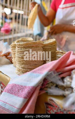 Ein Haufen frisch zubereiteter Tortillas auf der Theke neben einer anonymen Köchin, die tagsüber auf dem lokalen Markt arbeitet Stockfoto