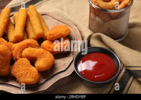 Leckeres Ketchup, Hähnchennuggets und Käsesticks auf beiger Tischdecke, Nahaufnahme Stockfoto