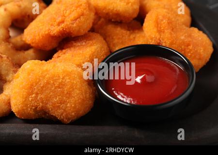 Leckeres Ketchup und Hähnchennuggets auf schwarzem Teller, Nahaufnahme Stockfoto