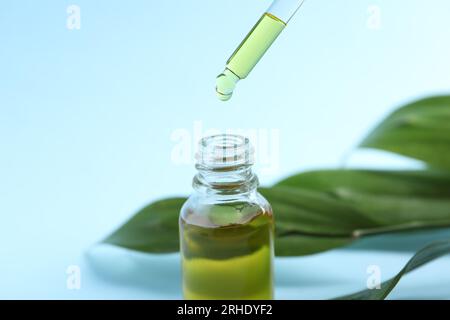 Tropfendes kosmetisches Öl von der Pipette in die Flasche auf hellblauem Hintergrund, Nahaufnahme Stockfoto