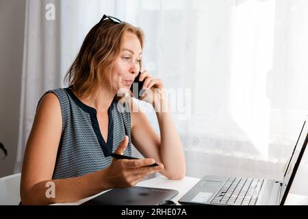 Remote-Arbeit. Die Frau arbeitet zu Hause am Computer und telefoniert. Das Konzept von Quarantäne, Freiberufung und Selbstisolation. Stockfoto