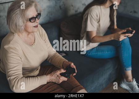 Emotionaler Großmörder, der Videospiele auf Gamepads spielt, Spaß hat. Großmutter der Seniorin gewinnt das Spiel und freut sich über den Sieg. Stockfoto