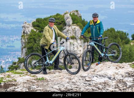 16. August 2023, Bayern, Aschau Im Chiemgau: Joachim Herrmann, (l, CSU) Staatsminister des Innern, für Sport und Integration, und Klaus Stöttner, MDL und erster Vorsitzender des Bayerischen Kuratoriums für Alpensicherheit e. V., stehen bei einer Ernennung für die Medien auf dem Kampenwand zusammen mit Elektrofahrrädern. Herrmann sammelte Informationen über den Kampenwand zu den Themen alpenunfallstatistik, "sicheres Mountainbiking" und "Sicherheitsausrüstung für Via ferrata". Es gab auch eine Demonstration eines Bergrettungsdienstes mit einem Helikopter, der als Operninstrument unverzichtbar ist Stockfoto