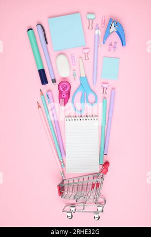 Schul- und Bürobedarf mit Warenkorb auf pinkfarbenem Hintergrund, Modellansicht von oben, Einkaufskonzept Nahaufnahme Stockfoto