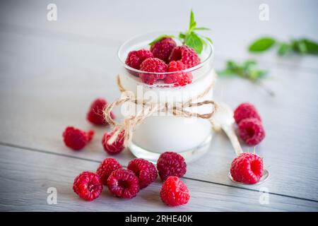 Gekochter hausgemachter Joghurt mit Reifen roten Himbeeren in einem Glas auf einem Holztisch. Stockfoto