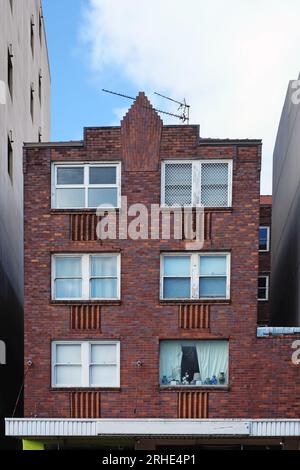 Ein kleines 3-stöckiges Art déco-Apartmentgebäude aus rotem Backstein mit Ziegelkammern unter doppelt hängenden Fenstern, ein zentrales Ziegelwappen bricht die Attika. Stockfoto