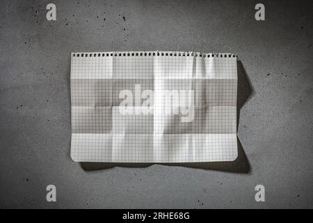 Zerknitterte Notizbuchpapierseite auf dunkler Betonoberfläche. Hintergrund mit Papierstruktur und Kopierraum Stockfoto