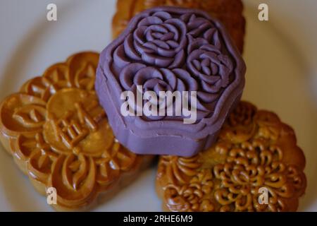 Ein lilafarbenes Taro-Gebäck mit Blumen sitzt auf drei Biskuit-farbigen Mondkuchen auf einer weißen runden Platte, die Details zeigt Stockfoto