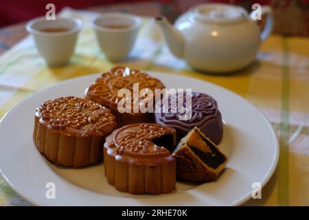 Mitte des Herbstmonds, eine Auswahl von vier chinesischen Mondkuchen auf einem weißen Teller, ein Viertel entfernt mit schwarzem Sesam und rundem Eigelb. Stockfoto