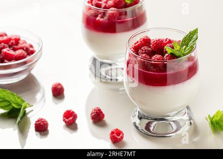 Panna Cotta mit Himbeergelee und Minzblättern in Glasgläsern auf einem weißen Tisch. Stockfoto