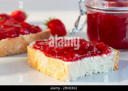 Weizenbrot mit aufgestrichener Erdbeermarmelade auf dem Tisch. Stockfoto