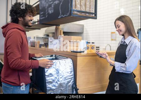 Ein männlicher Kurier mit Lockenhaar nimmt Befehle aus dem Café entgegen Stockfoto