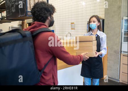 Ein männlicher Kurier mit Lockenhaar nimmt Befehle aus dem Café entgegen Stockfoto