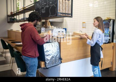 Ein männlicher Kurier mit Lockenhaar nimmt Befehle aus dem Café entgegen Stockfoto