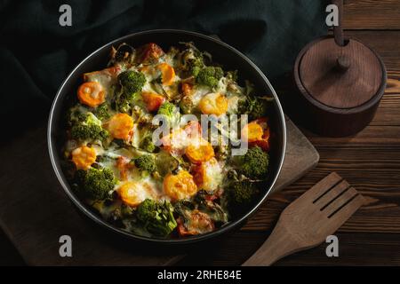 Mit Brokkoli, Karotten und Käse im Ofen auf einem dunklen Holztisch gratin. Stockfoto