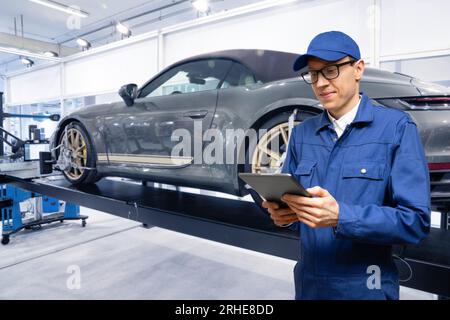 Servicemänner mit digitalem Tablet auf dem Hintergrund des Autos im Autodienst. Stockfoto