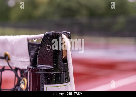 Oberseite des schwarzen Tennisplatznetzpfostens mit weißem Kabel und Messing-Spannführung. Stockfoto