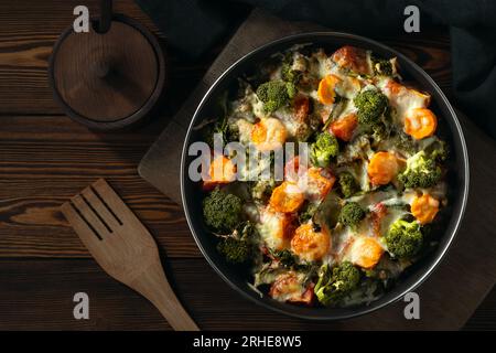 Mit Brokkoli, Karotten und Käse im Ofen auf einem dunklen Holztisch gratin. Stockfoto