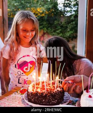 Happy Girl bläst festliche Kerzen auf ihrem Geburtstagskuchen aus Stockfoto