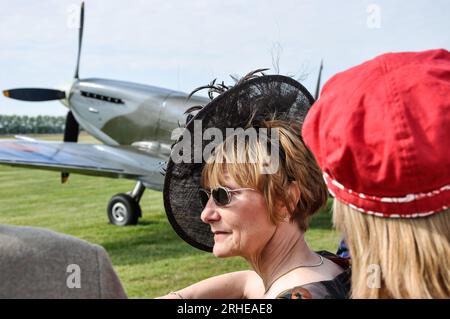 Weibliche Kleidung aus dieser Zeit, die die Luftausstellung beim Goodwood Revival Vintage Event in West Sussex, Großbritannien, beobachtet. Spitfire-Flugzeug. Schicker schwarzer Hut, Fascinator Stockfoto