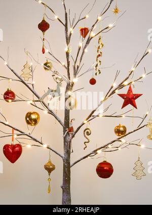 Weihnachtsbaumschmuck in traditionellem Rot und Gold hängt an einem modernen Zweig mit Schnee-Effekt Stockfoto