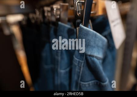 Verschwommenes Foto von Jeanshosen im Bekleidungsgeschäft. Jeans am Kleiderbügel, die im Bekleidungsgeschäft auf dem Regal hängen. Modegeschäft im Einkaufszentrum. Kleidung Stockfoto