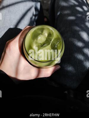 Grüner Tee-Smoothie, schmücken Sie das Topping mit Schlagsahne in einem klaren Glas auf einem Zerkleinerer mit dunkelgrauem Echtholzboden. Beliebtes Getränk, um den Durst zu stillen Stockfoto