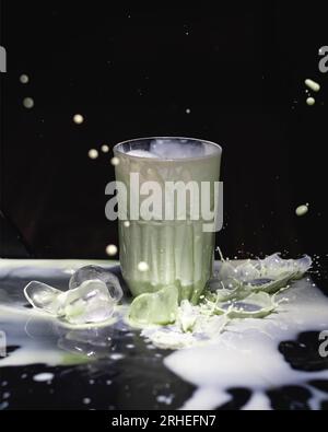 Grüner Matcha mit Sahne auf schwarzem Hintergrund, während Milch verschüttet und Eis geworfen wird, kaltes Getränk mexiko lateinamerika Stockfoto