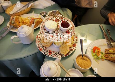 Butterscones mit Marmelade und Clotted Cream, serviert mit Schinken-Käse-Sandwiches und Teekannen Stockfoto