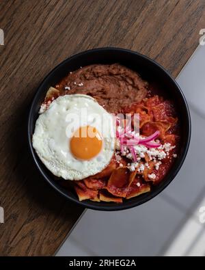 Herzhaftes Frühstück mit Rührei, Speck, Bohnen, Kirschtomaten, hausgemachtem Brot, Orangensaft auf einer Betonplatte. Englisches Frühstückskonzept. Stockfoto
