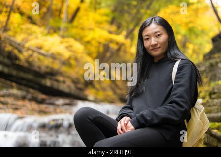 Eine chinesin sitzt in der Nähe eines Wasserfalls im Buttermilk Falls State Park in Ithaca New york im frühen Herbst. Stockfoto