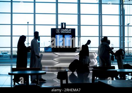 Flughafen Bahrain. Passagiere, die in Silhouette vorbeifahren, mit Hintergrundbeleuchtung. Informationsschalter Stockfoto