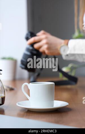 Frau, die eine Fotokamera in der Nähe einer Holzscheibe hält, mit einer Tasse Kaffee Stockfoto