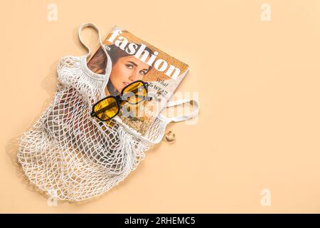 Stilvolle Sonnenbrille und Tragetasche mit Zeitschrift auf beigefarbenem Hintergrund Stockfoto